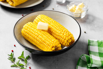 Cooked corn on the cob served with salt and butter. Light gray background.