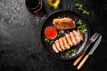 Roasted duck breast served with sauce and fresh herbs. Black background. top view