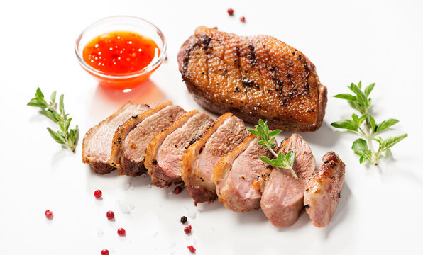 Roasted duck breast served with sauce and fresh herbs. White background