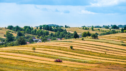Fototapeta na wymiar Beautiful view on an agricultural field in the time of harvest. Flat hills, trees on the horizon. Harvester machine in the foreground. Sunny, summer day in Zwierzyniec, Roztocze, Poland.