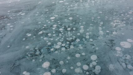 Turquoise ice, close-up. Full screen. Intersecting cracks are visible on the surface. Columns of frozen methane gas go deep. Baikal