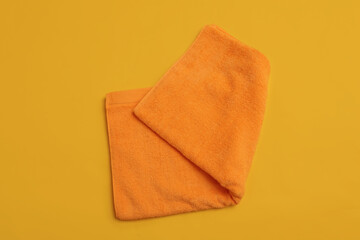 Folded orange beach towel on yellow background, top view