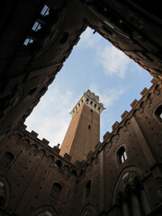 In Siena, Tuscany, Italy, the Torre del Mangia clock tower, built in 1348, is shown from below, in the courtyard of Palazzo Pubblico (Town Hall) during the day.