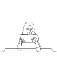 woman holds a tablet horizontally in her hands - one line drawing. long haired female user looks at the screen of her tablet, which she holds in front of her