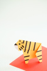 白い背景に赤い敷物の上に折り紙の横向きの黄色い虎縦構図