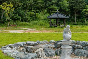 Dry stone circled water fountain with tiled roof gazebo in background.