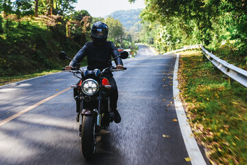 Obraz premium Man in a black helmet rides classic motorcycle on the road among autumn forest. Lifestyle or hobby of grown up man
