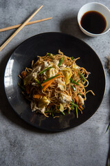 Schezwan noodles prepared with chopped vegetables, meat and udon noodles in a white plate. View from top. 