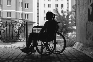 The girl is sitting in a wheelchair on a gray background. The concept of bias towards disabled...