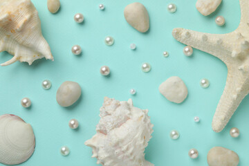 Beautiful sea shells, starfish, pearls and pebbles on light blue background, flat lay