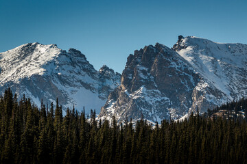 A wide angle landscape shot of dramatic, snowy mountain peaks covered in snow with pine trees, an outdoor winter background