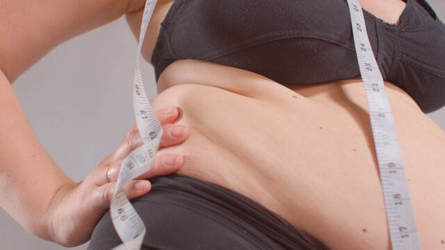 Fat folds on the woman's sides. A measuring meter hangs on the shoulder. Awareness about weight gain. A quick set of calories. Overweight.