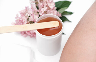 sugaring paste and spatula next to female leg. flowers on a background. depilation at home, skin and body care. hair removing.