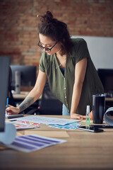 Interior designer or architect in casual wear with messy hairdo making notes while working on new project, standing in her office on a daytime