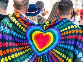 Two men with a raimbow flag with colored hearts on their backs at LGBTQ Pride parade in Bucharest,...