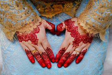 Selective focus and close-up shot of bride's hand. Bride makes a heart shape with a red henna...