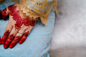 A close-up shot of bride's hand with red henna tattoo and wedding ring. 