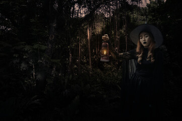 Obraz na płótnie Canvas Halloween witch holding ancient lamp standing over dark forest and tree, Halloween mystery concept