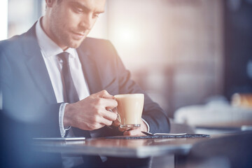 Confident young man in full suit enjoying coffee while sitting in the restaurant