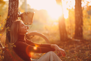 Happy active young woman sitting near vintage bicycle bike in autumn park at sunset. European...