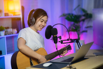 Beautiful girl singing with headphone and playing guitar recording new song with microphone in the...
