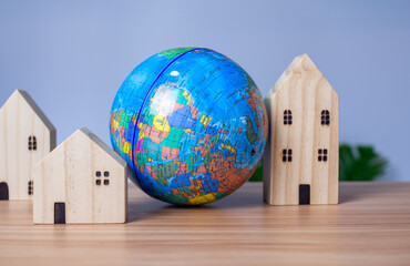 A wooden model house is placed beside a replica globe. placed on a wooden table with a light gray...
