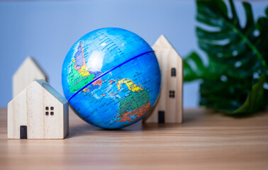 A wooden model house is placed beside a replica globe. placed on a wooden table with a light gray background. save world concept