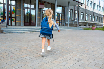 Naklejka premium Cute little girl with backpack running back to school. Back rear view little schoolar in grey dress uniform going to elementary school.