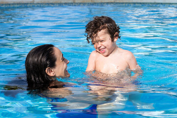 Mother and son bathing in the pool,both of them smiling happily looking at each other while enjoying