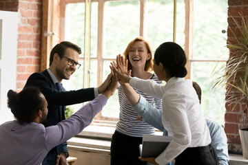 Group of happy colleagues accomplish meeting or start new project feel motivated giving high five, diverse staff celebrate teamwork results and business growth. Members engaged in teambuilding concept