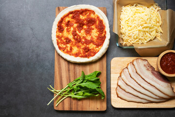 Pizza dough with ingredients on wooden board with black table background. Homemade delicious pizza. Top view and copy space.