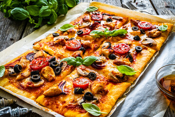 Pizza with white mushrooms, chicken nuggets, tomatoes, black olives and mozzarella on wooden background
