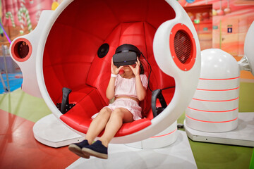 Young girl wearing virtual reality googles and experiencing virtual reality in moving interactive...