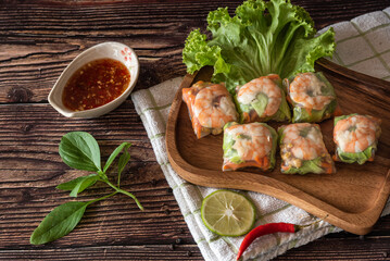 Top view of Asian fresh spring rolls with pork and shrimp, serve with spicy sauce, Thai traditional food on wooden background 