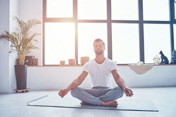 Handsome young man doing yoga while sitting in lotus position at home