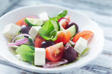 Healthy salad with feta cheese, kalamata olives, cherry tomatoes and fresh basil. Bright wooden background. Close up. 	