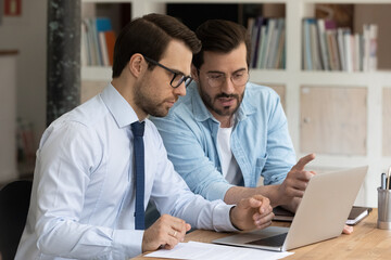 Two serious, confident male office colleagues review collaborative corporate task, discussing...
