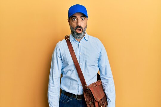 Middle age man with beard and grey hair wearing delivery courier cap afraid and shocked with surprise expression, fear and excited face.
