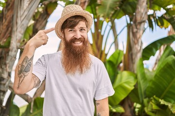 Caucasian man with long beard outdoors on a sunny day wearing summer hat smiling happy pointing with hand and finger