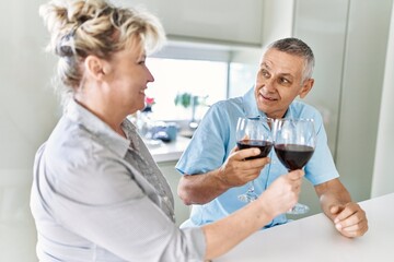 Fototapeta premium Senior caucasian couple smiling happy toasting with wine at the kitchen.