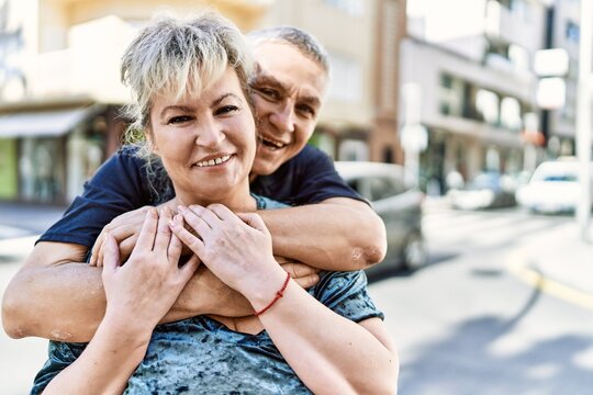 Middle age caucasian couple of husband and wife together on a sunny day outdoors. Smiling happy in love hugging at the city.