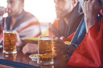 Close-up of young men covered in international flags enjoying beer