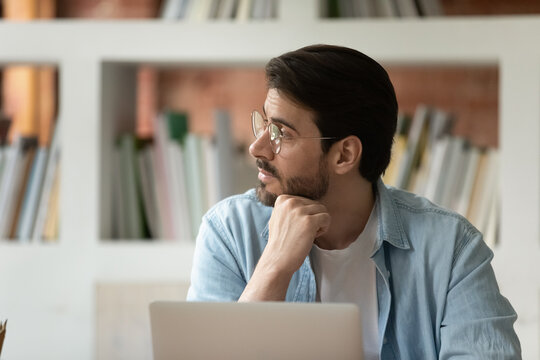 Concerned thoughtful businessman or student in glasses sit at desk with laptop lost deep in thought looks away thinking solving problem at work, hard task, search solution, business challenge concept