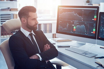 Thoughtful young man in shirt and tie analyzing data on the stock market while working in the office