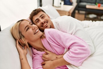 Young caucasian couple smiling happy and hugging lying on the bed at home.
