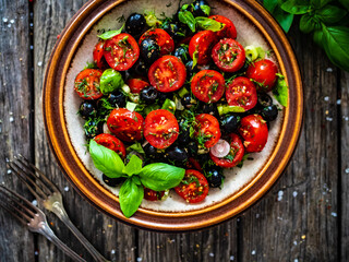 Fresh vegetable salad with cherry tomatoes, black olives, dill,  basil  and garlic on wooden table