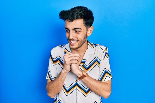 Young hispanic man wearing casual clothes laughing nervous and excited with hands on chin looking to the side