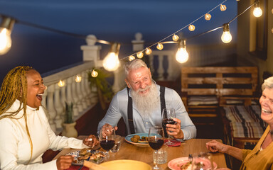 Happy multiracial senior friends having fun dining together on house patio - Elderly lifestyle...