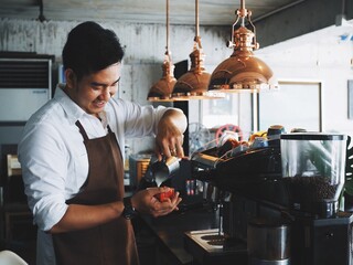 Attractive Asian man making coffee in his cafe.