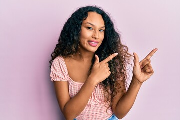 Young latin woman wearing casual clothes smiling and looking at the camera pointing with two hands and fingers to the side.